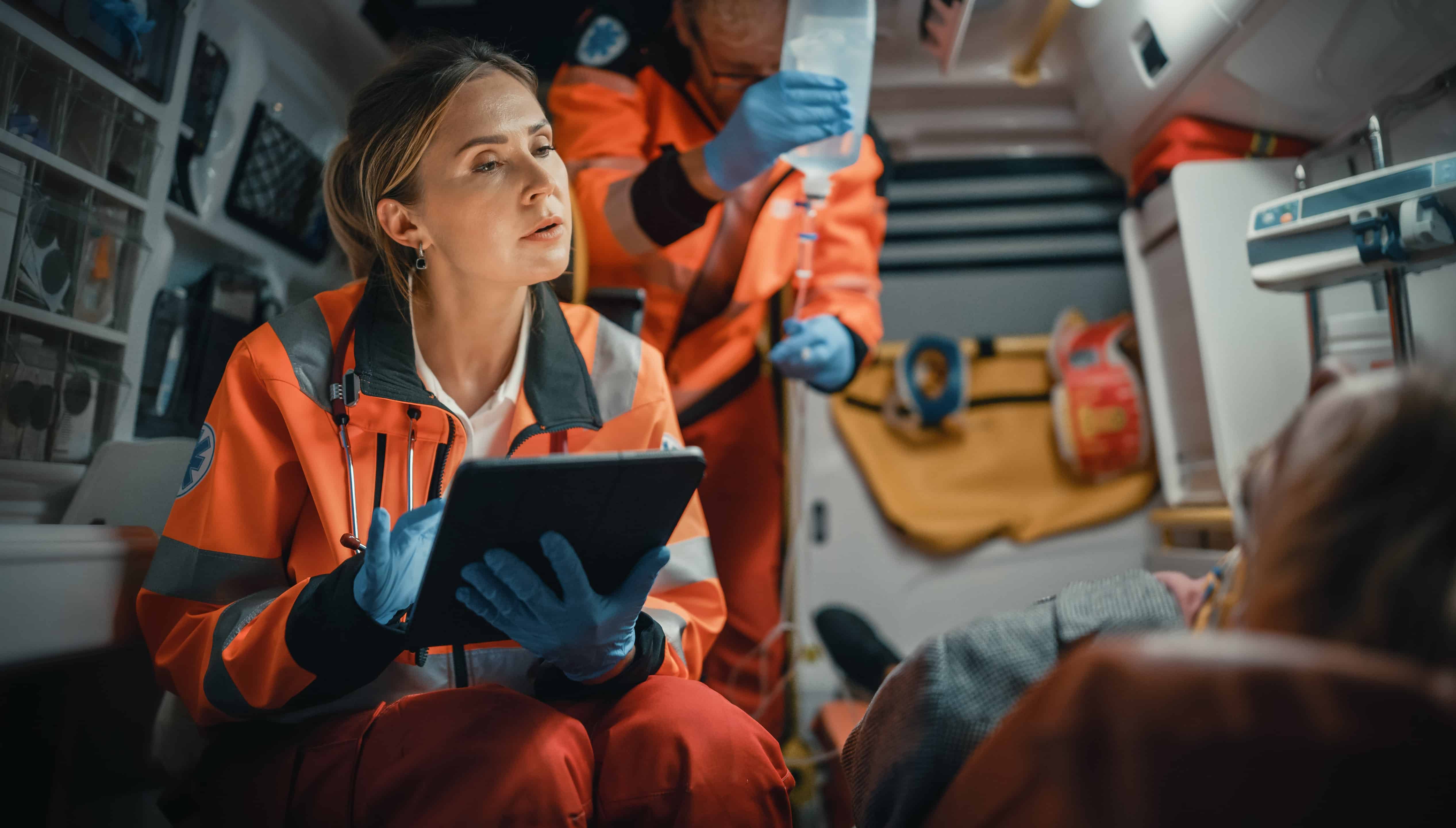 Female EMS professional using a tablet and speaking with a person